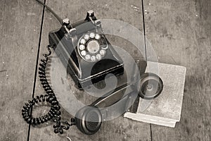 Retro black telephone and books on old oak wooden table. Vintage style sepia photo