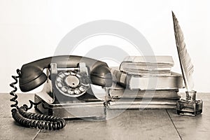 Retro black telephone, books, quill and inkwel on old oak wooden table. Vintage style sepia photo