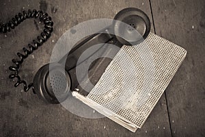 Retro black telephone handset and book on old oak wooden table. Vintage style sepia photo