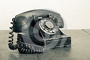 Retro black telephone on old oak wooden table. Vintage style sepia photo