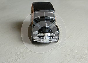 Retro black toy car on gray striped surface. Model of classic vintage sport car with shadows and partly soft focus. Front view of