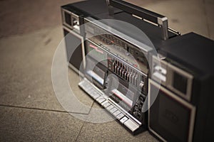 The retro boombox, an outdated portable radio with a cassette recorder from the 80s, stands on the sidewalk. Rap, hip