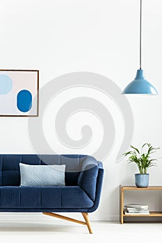 Retro bowl pendant light and a baby blue cushion on a dark, elegant sofa in a simple living room interior with white walls. Real p