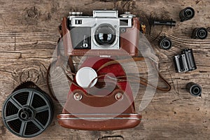 Retro camera in a brown leather case lies on a wooden table. Top view