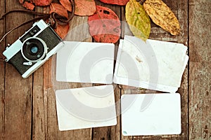 Retro camera and empty old instant paper photo album on wood table with maple leaves in autumn border design