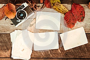 Retro camera and empty old instant paper photo album on wood table with maple leaves in autumn border design