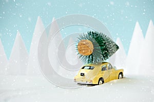 Retro car toy carrying Christmas fir tree in snowy landscape. Christmas or New Year celebration concept. Copy space. Selective