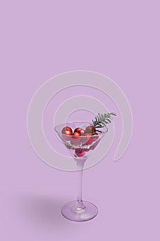 Retro Christmas party concept. Martini glass full of small red Christmas ornament with green little spruce. Violent velvet