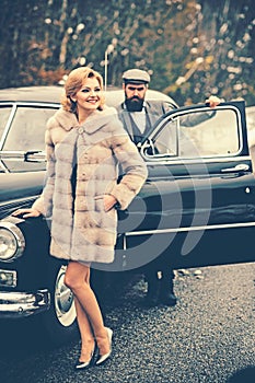 Retro collection car and auto repair by mechanic driver. Bearded man and sexy woman in fur coat. Escort of girl by