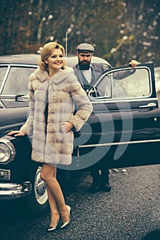 Retro collection car and auto repair by mechanic driver. Bearded man and sexy woman in fur coat. Escort of girl by