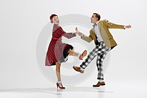 Retro dance scene with young stylish man and beautiful woman in red dress dancing joyously isolated over white studio photo