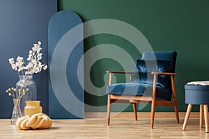 Retro dark blue armchair in elegant, living room interior with copy space on empty green and blue wall