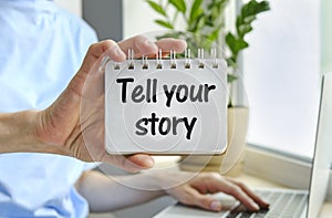 Retro effect and toned image of a woman hand writing a note with a fountain pen on a notebook. Handwritten text Tell Your Story as