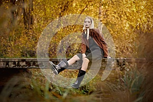 Retro fashion woman in boots sitting on a bridge