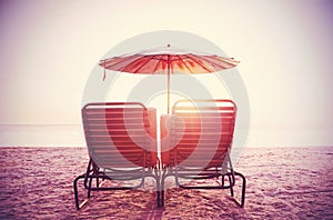 Retro filtered picture of beach chairs and umbrella on sand.