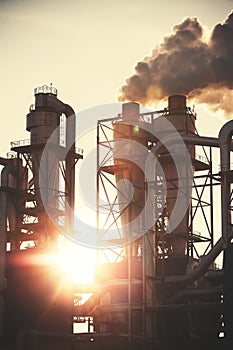 Retro filtered picture of smoky chimneys silhouettes against sun.