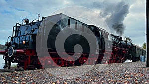 Retro German coal steam locomotive with thick clouds of steam leaving station