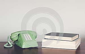 Retro green telephone on wood table with book vintage tone