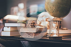 Retro hourglass, blur stack of old books and world desk globe on wooden table