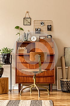 Retro interior design of art workshop room with wooden vintage bureau and chair, cube, plants, cacti, books, photos.