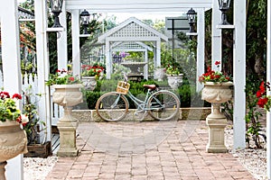 Retro ladies bicycle with basket standing against garden retaining brick wall, underneath white wooden pergola with lush green shr