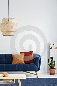 Retro lampshade above a simple, wooden coffee table on a navy blue rug in a colorful living room interior with pillows on a couch.