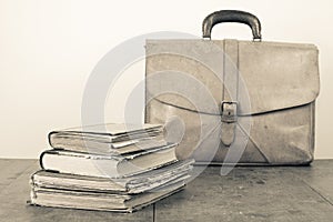 Retro leather bag and aged books on oak wooden table. Vintage style sepia photo