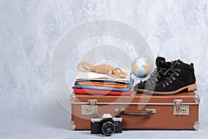 Retro leather suitcase with travel accessories on grey background. Stack of clothes, film photo camera, suede shoes, globe. Travel