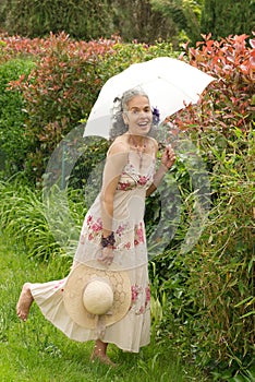 Retro mature woman laughing in garden with umbrella