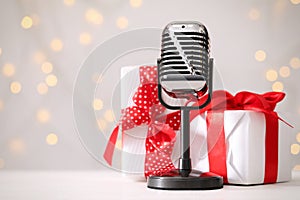 Retro microphone and gift boxes on table against blurred lights, space for text. Christmas music