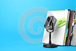 Retro microphone, notebooks and reminder note with words JOB INTERVIEW on light blue background
