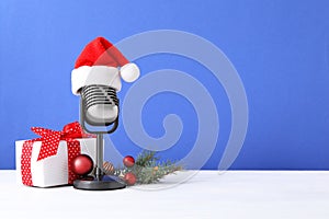 Retro microphone with Santa hat, gift box and festive decor on table against blue background, space for text. Christmas music