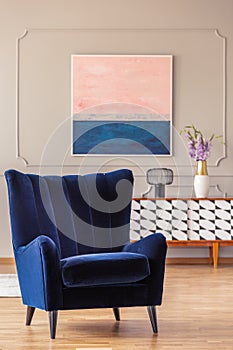 Retro, navy blue armchair in an elegant living room interior with an abstract painting on a wall