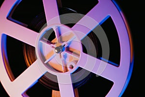 Retro old-fashioned 8mm projector playing reels with tape film. Close-up of coil turning under colorful light. Vintage