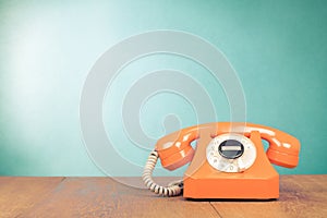 Retro orange telephone on wooden table in front gradient mint blue background. Vintage style photo