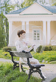 Retro photo of a beautiful woman in a golden dress who writes a letter with a quill pen in the garden