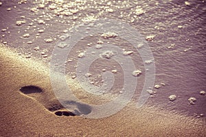 Retro picture of beach, water and footstep at sunset.