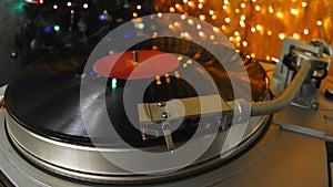 A retro player with vinyl records against the background and garlands of lights at a home Christmas party entertains a