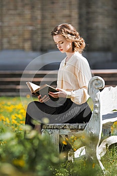 Retro portrait of a beautiful dreamy girl reading a book outdoors. Soft vintage toning.