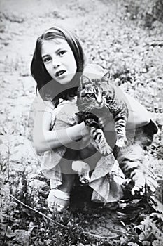 Retro portrait of Soviet girl with cat in hands. Vintage black and white paper photo. Early 1990s. Old surface, soft focus.
