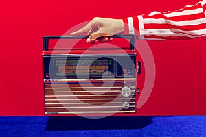 Retro radio. Female hand holding, touching radioreceiver  on blue and red background. Vintage, retro fashion