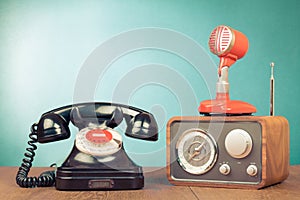 Retro radio, microphone and telephone on wooden table front mint blue background. Vintage style filtered photo