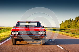 Retro red car standing on asphalt road at sunset