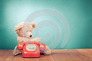 Retro red telephone and Teddy Bear front mint green wall background. Vintage style photo