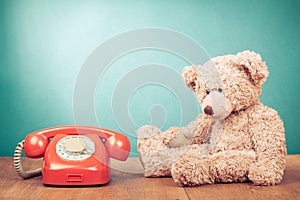 Retro red telephone and Teddy Bear near mint blue wall background. Vintage style photo