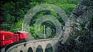 Retro red train moves along an old stone bridge. La Mure, France