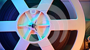 Retro reel with film rotating on sequins kinetic wall, colorful light. Old-fashioned 8mm projector playing in decorated