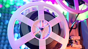 Retro reel with film rotating on sequins kinetic wall, colorful light. Old-fashioned 8mm projector playing in decorated