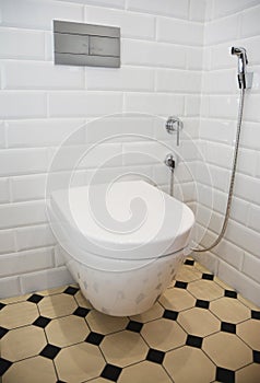 A retro renovated toilet room with white tiled walls, yellow and black vintage floor tiles, a wall mounted ceramic toilet bowl,