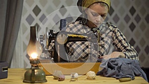 Retro seamstress girl sews cloth with old manual hand sewing machine. Woman works at home or workshop at night with
